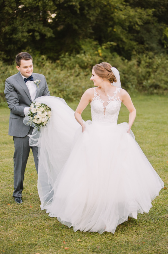 A candid photograph of a bride and groom, walking through a grass field